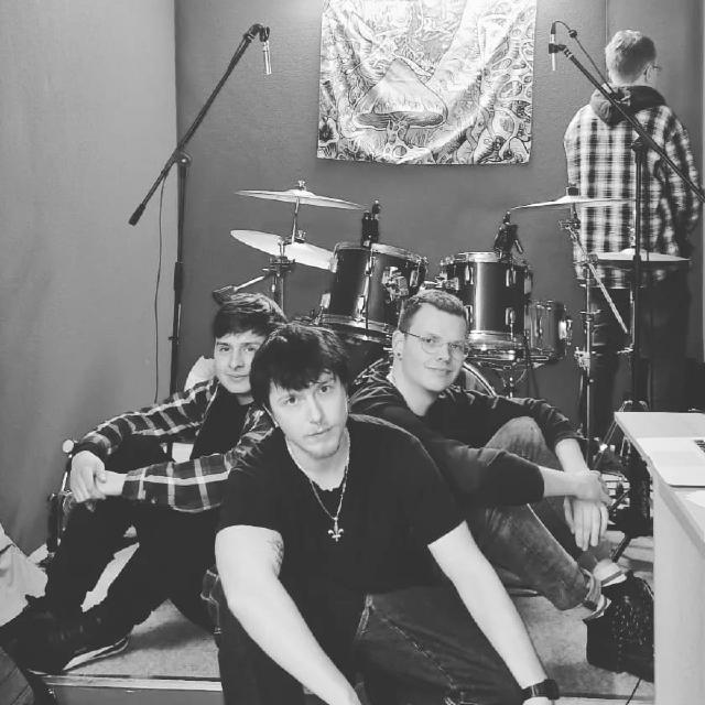 Vier Bandmitglieder im Proberaum, im Hintergrund ein Schlagzeug