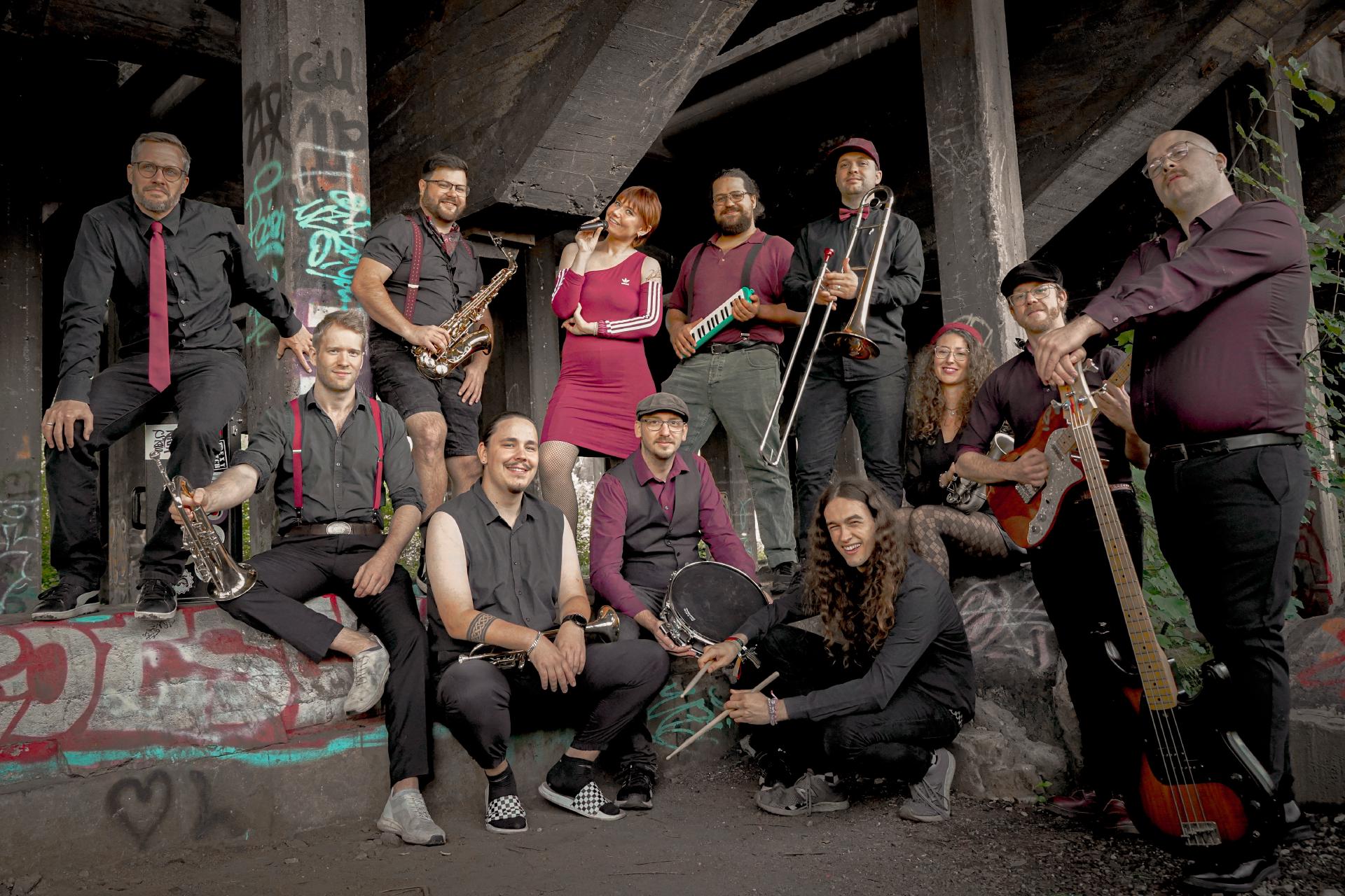 Die Band auf einem Industriegelände in ihrem Outfit, geprägt von der Farbe Schwarz und Bordeaux.