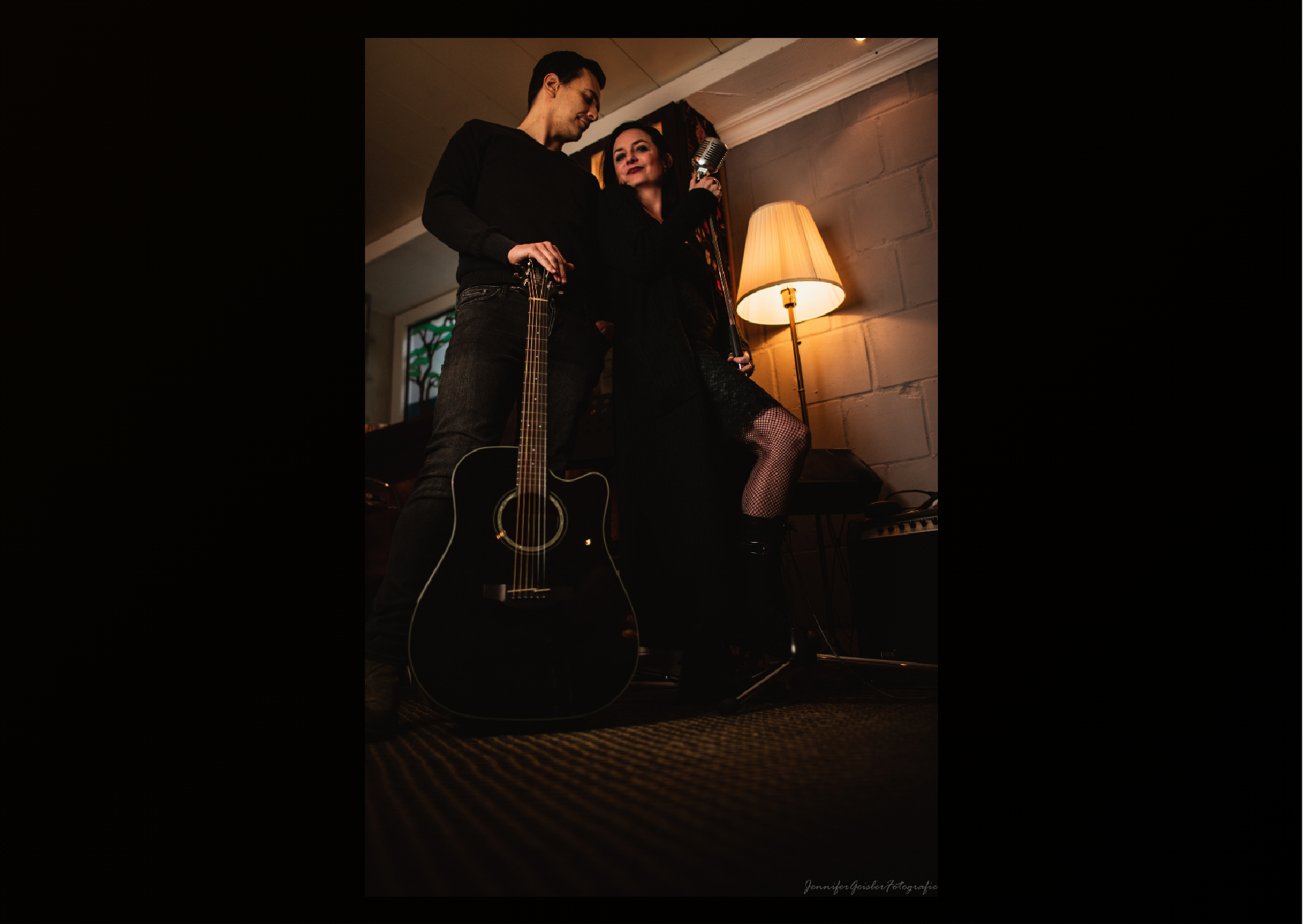 Zwei Personen stehen nah beisammen, warmes Licht, Gitarre und Mikrofon in den Händen.